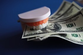 Tooth model gripping several hundred-dollar bills 