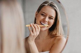 Woman brushing her teeth in front of bathroom mirror