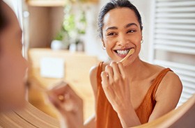 Happy woman brushing her teeth in front of bathroom mirror