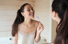 Young woman brushing her teeth in front of bathroom mirror